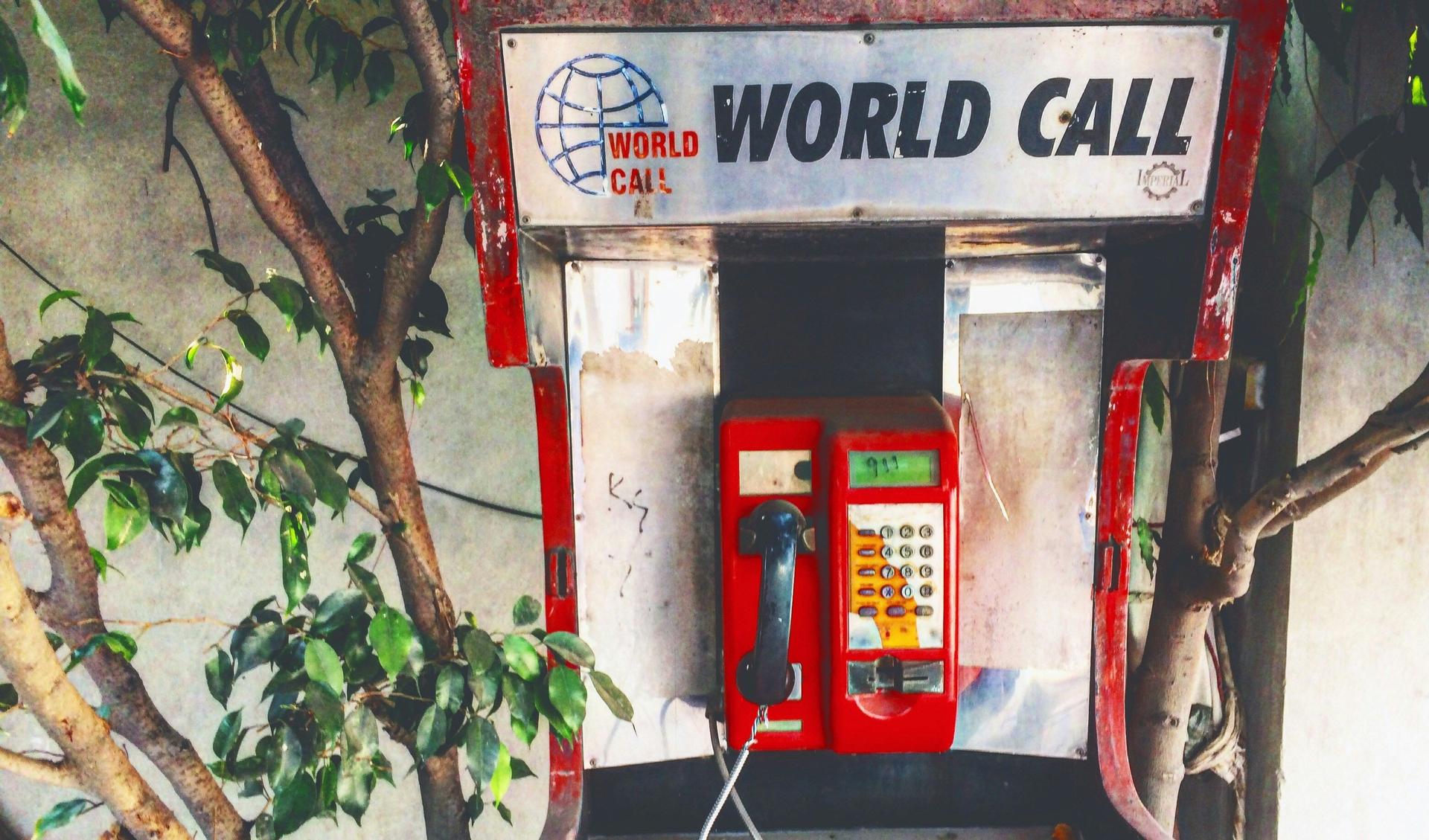 An old phone cell is mounted at a wall. It says World Call. On the screen someone painted 911.