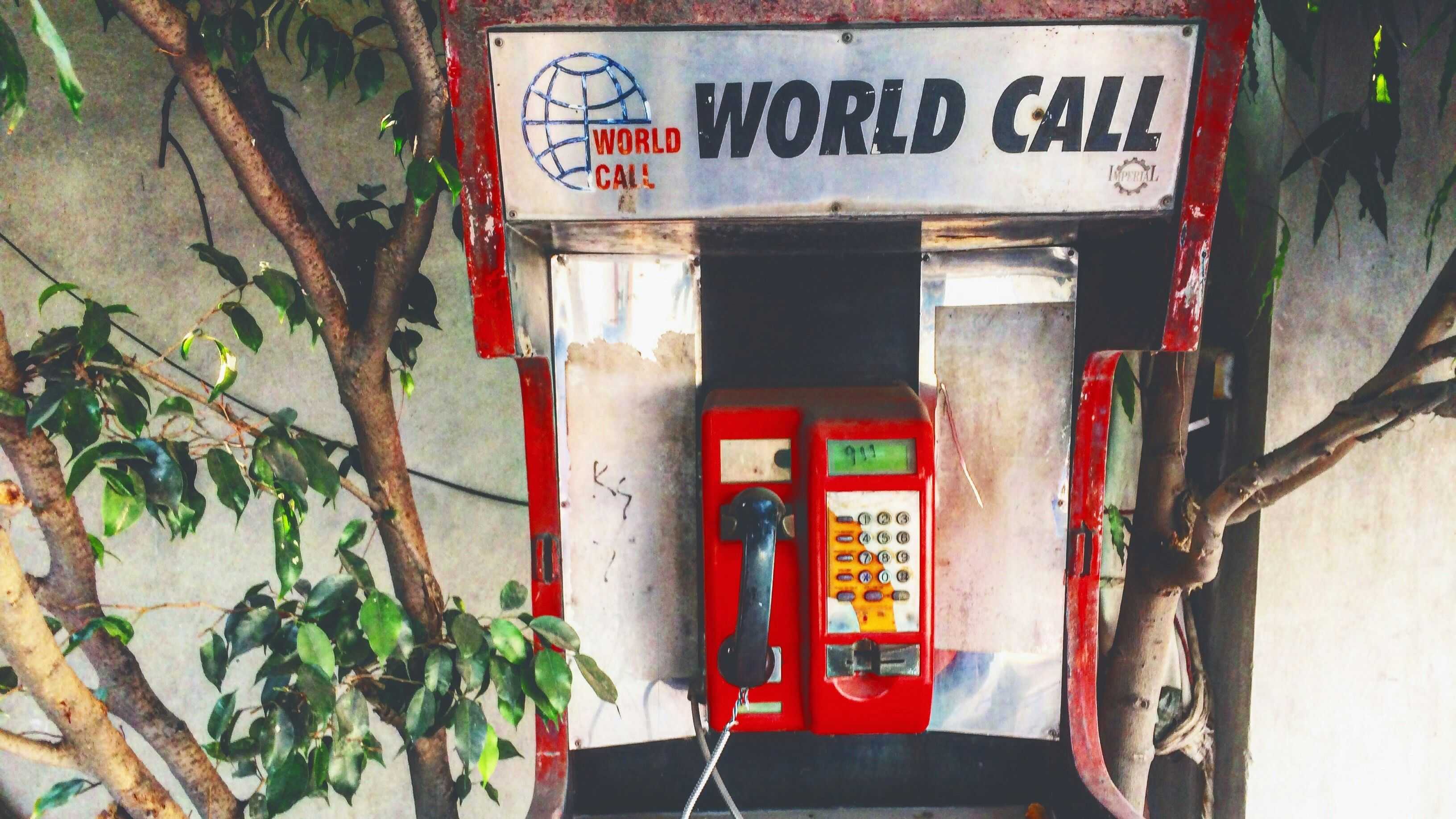 An old phone cell is mounted at a wall. It says World Call. On the screen someone painted 911.