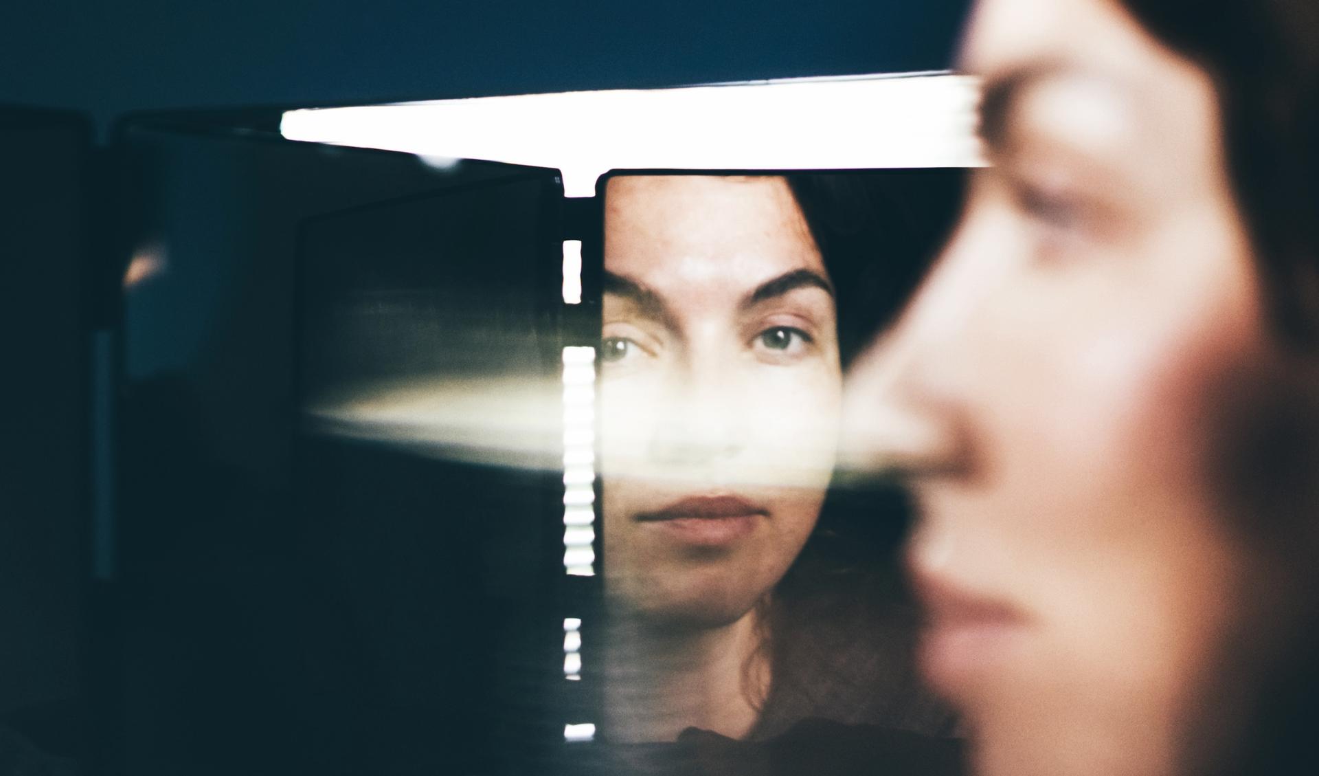 A person is looking away from a mirrow, while the reflection is looking at them. 