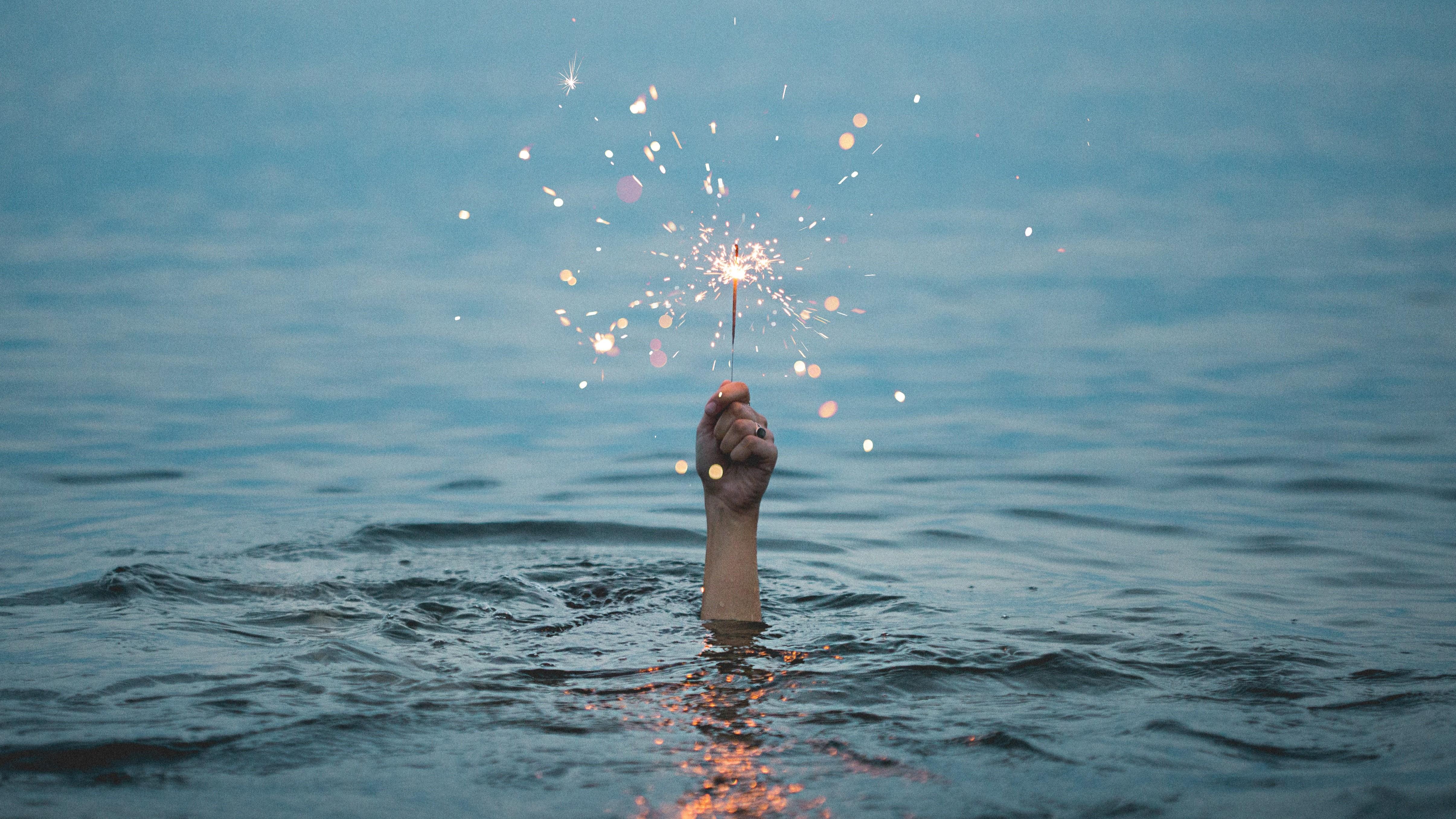 A hand coming out of the water holding  a sparkler