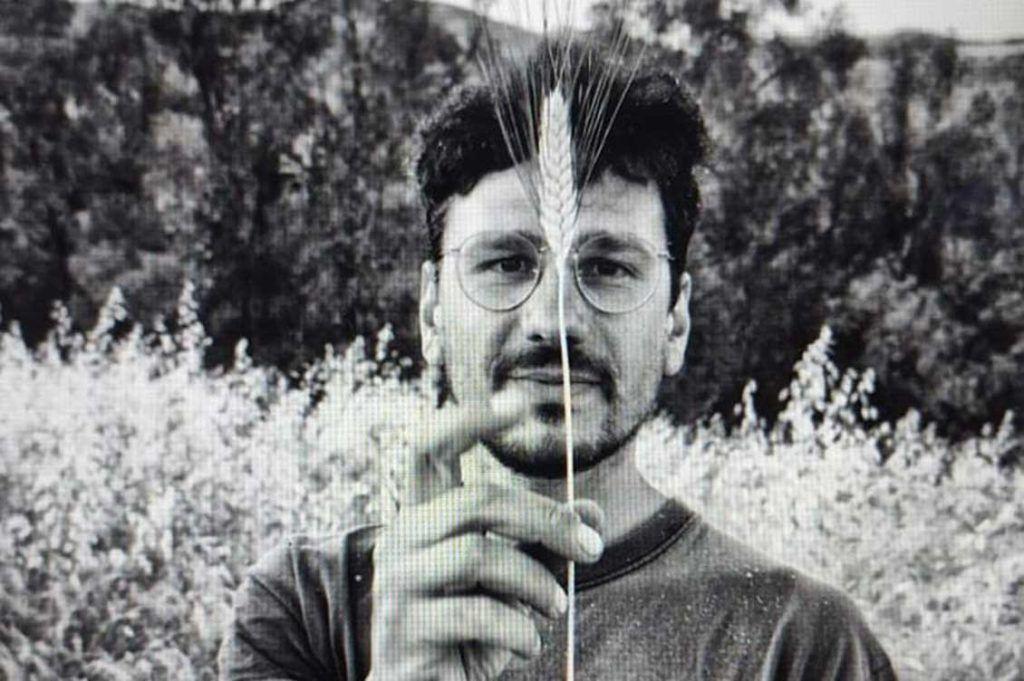 Piero is looking straight into the camera and is holding a grain leave in front of the face. The picture is black and white, Piero has short hair and wears glasses. 