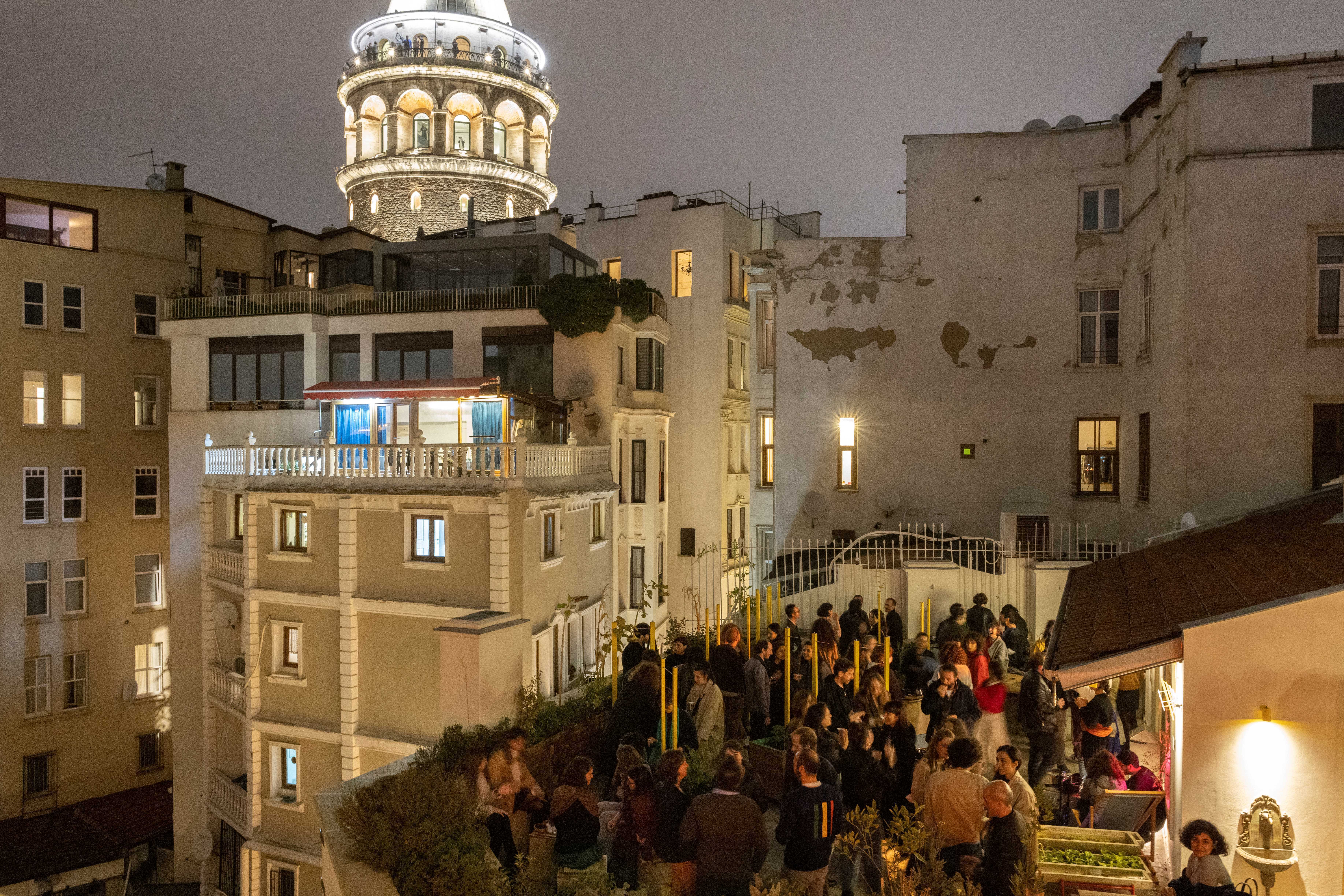 A terrace in the nightime in Istanbul is bustling. In the back you see Istanbuls houses