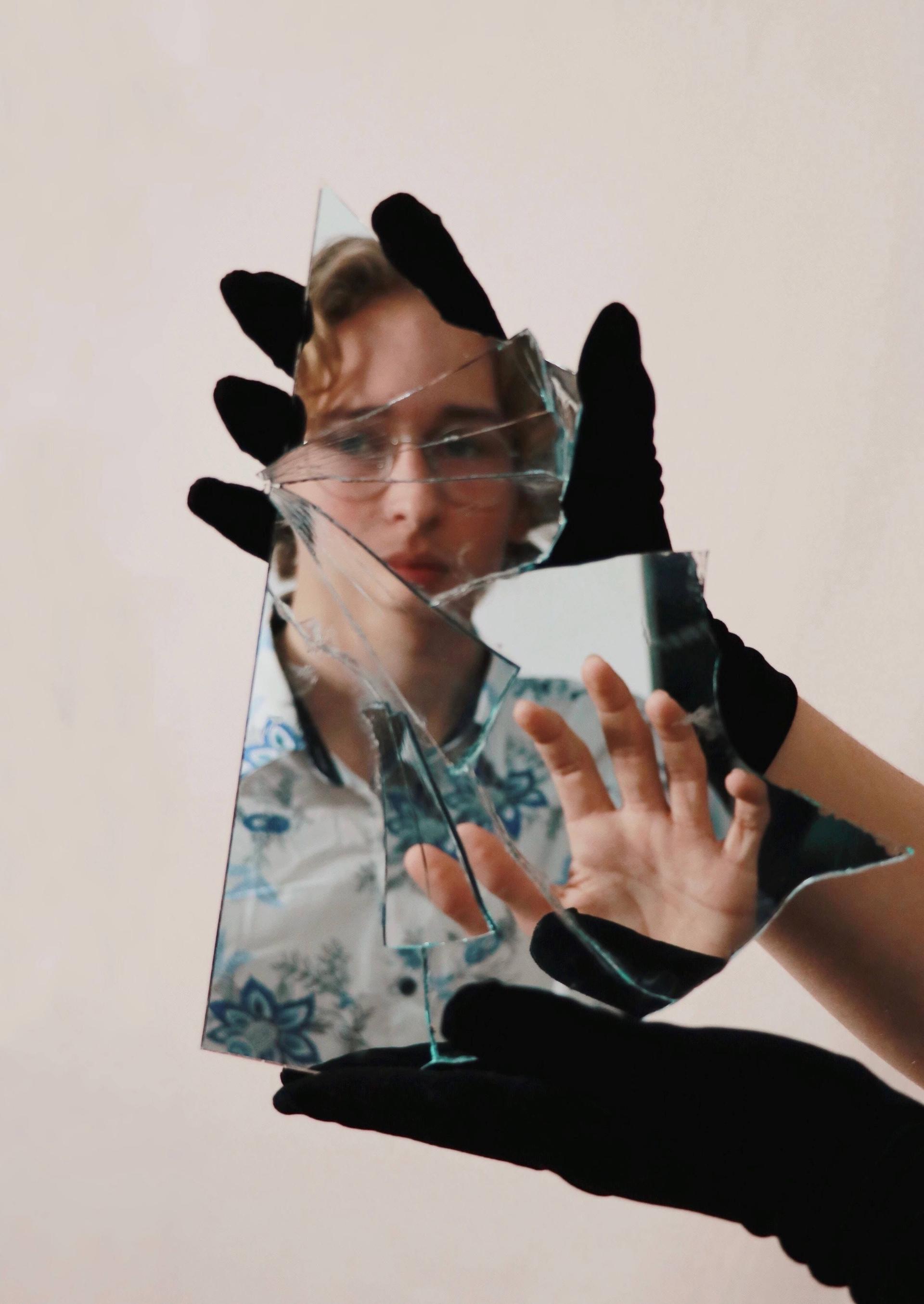 A person is looking into a piece of a mirror that another hand with black gloves is holding