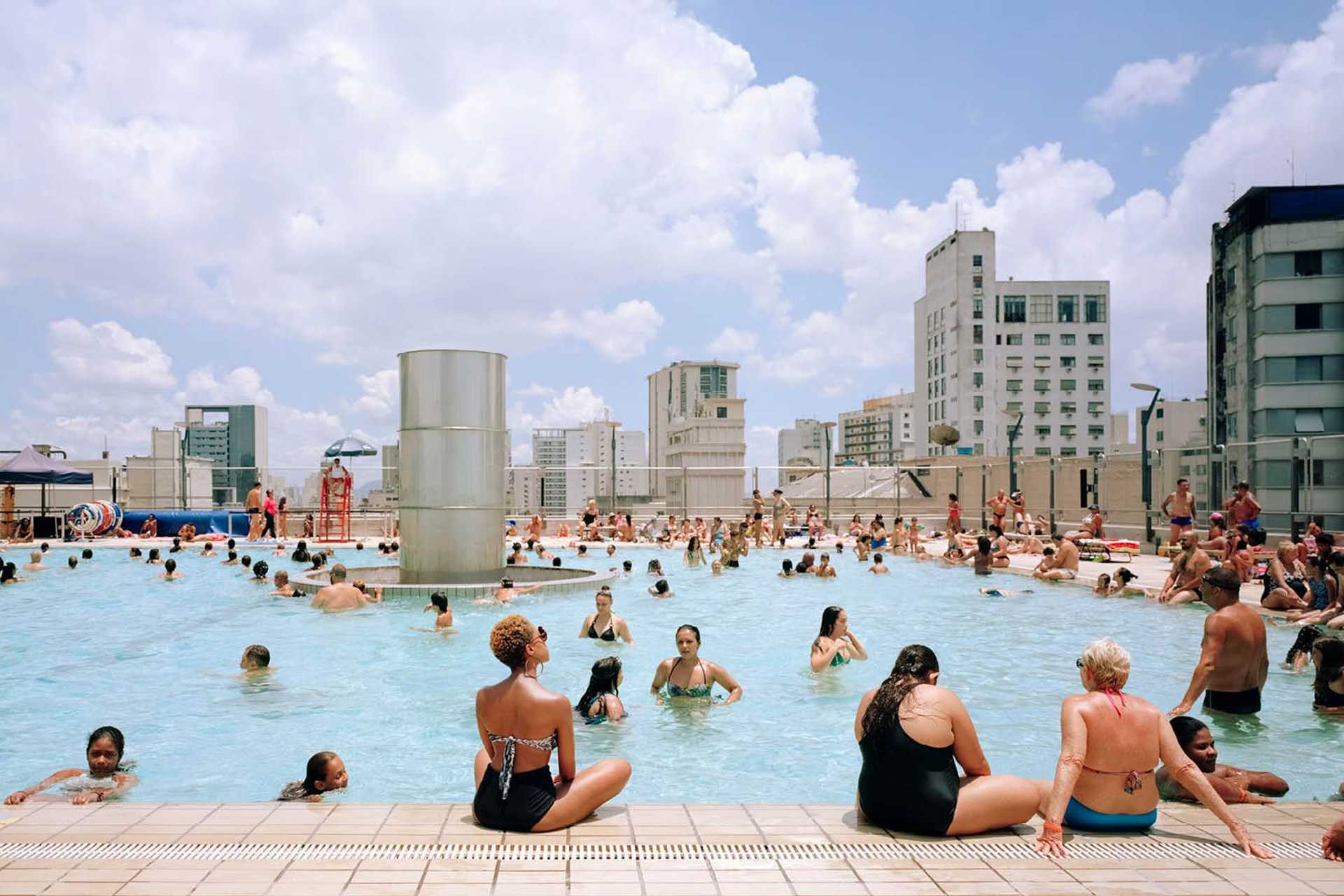 A swimming pool on a roof in Sao Paulo is showing people swimming and resting at the pool on the top of the city