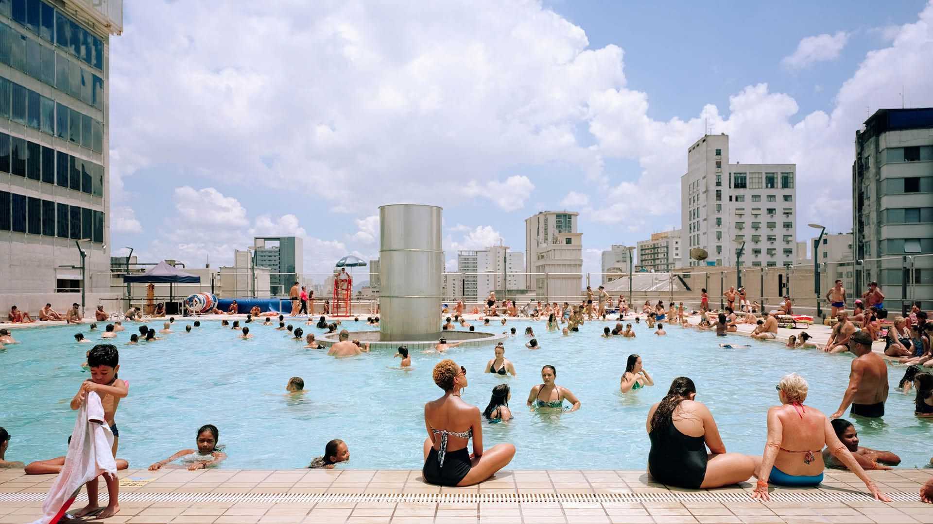 A swimming pool on a roof in Sao Paulo is showing people swimming and resting at the pool on the top of the city