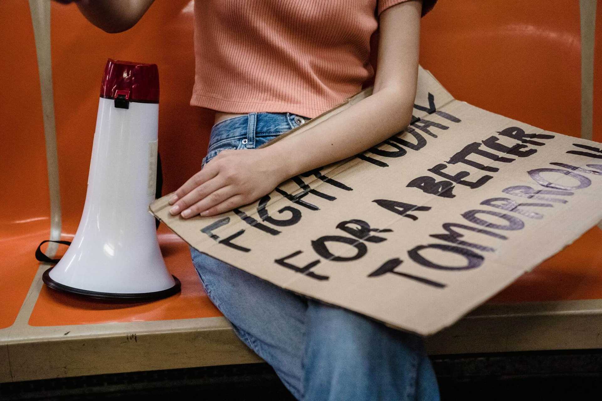 A person is sitting on a bench with a poster on her laps and a megaphone