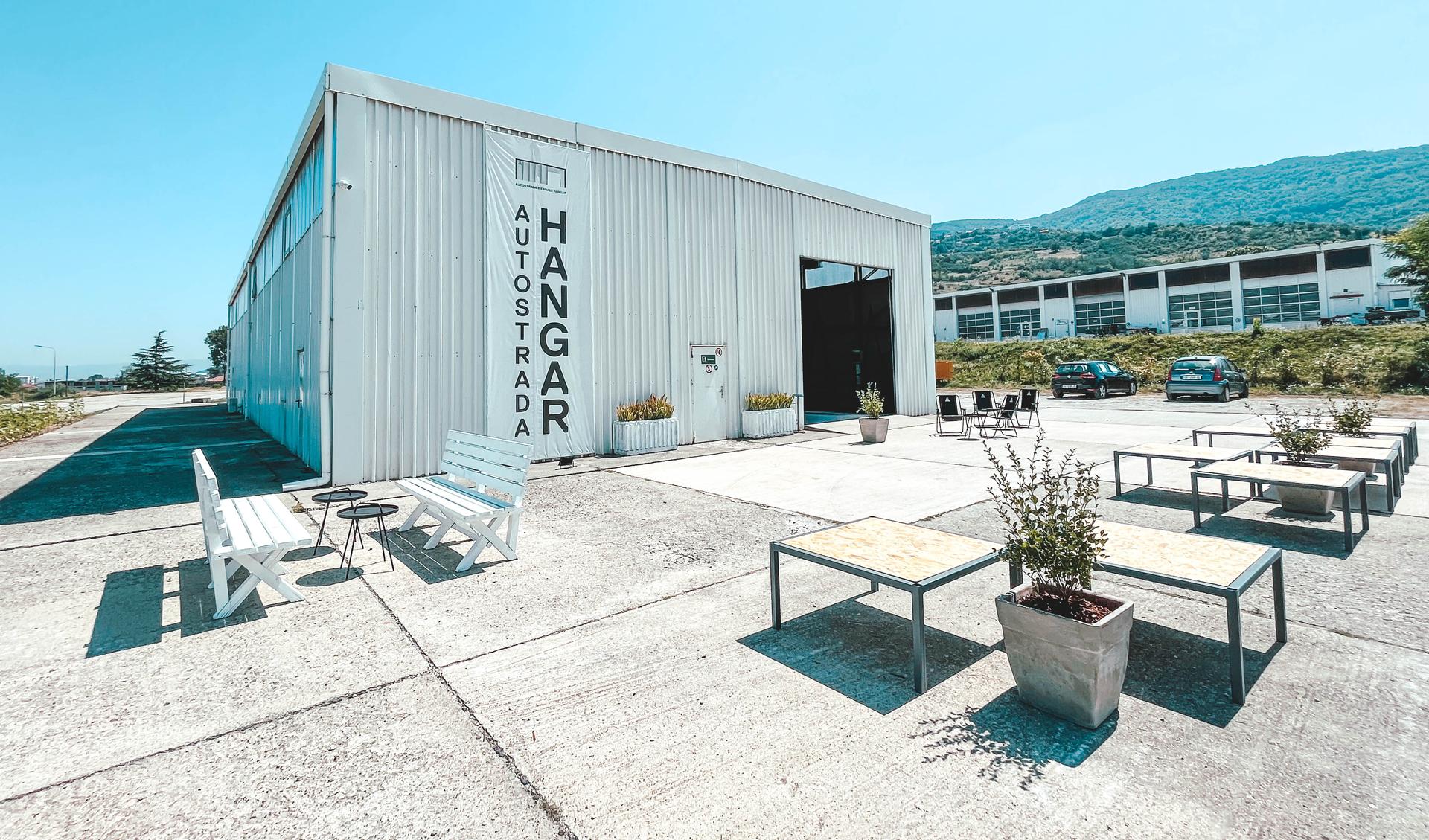 The hangar of Autostrada biennale. In fron you see an open air meeting spot with tables and benchesr 