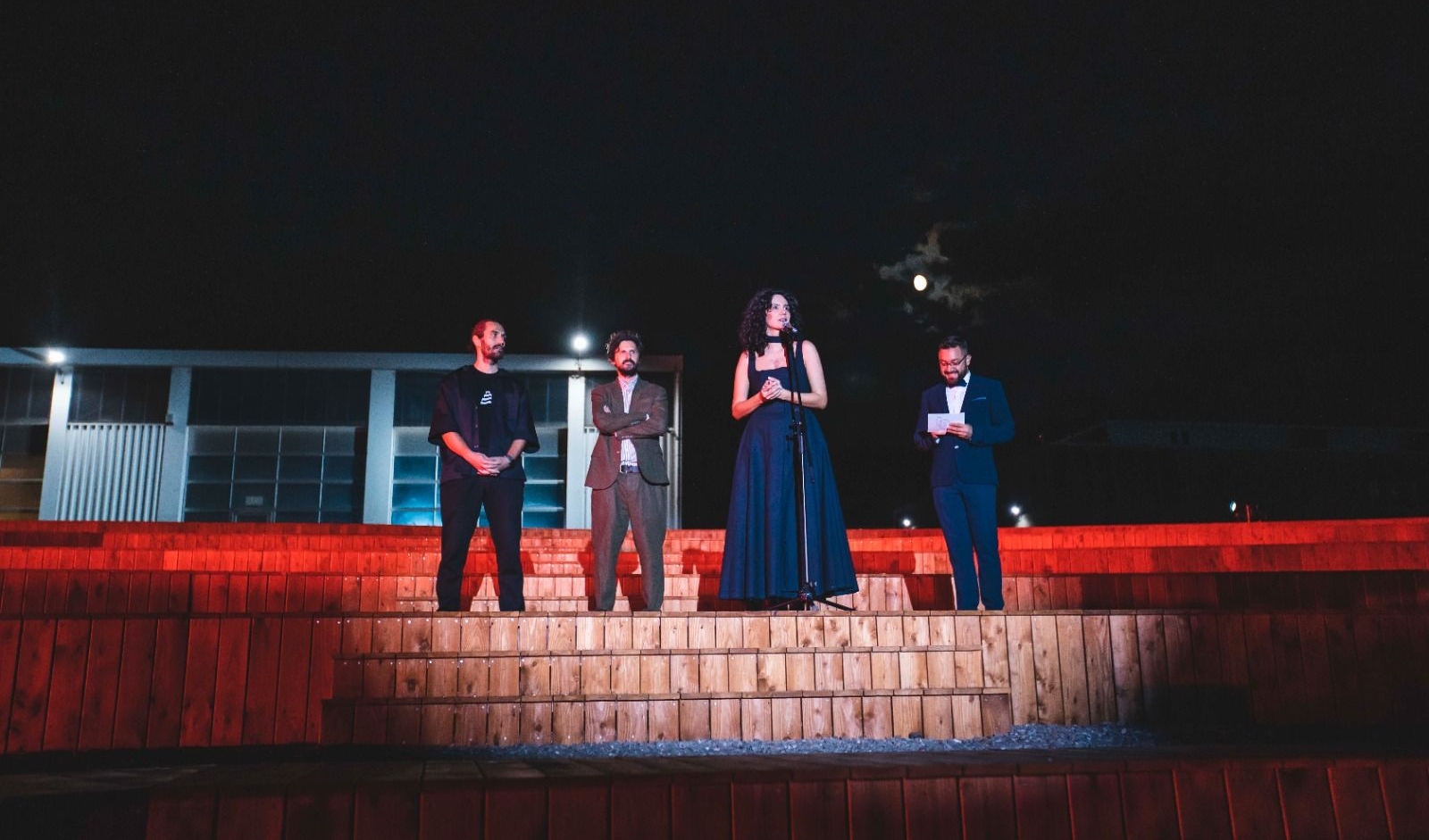 Four persons are standing, they are beautifully dressed and one of them is holding a speech