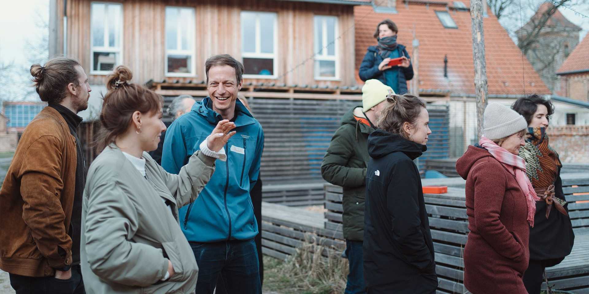 People are standing outside on a construction side in a smaller town oder village. They are talking to each other and are laughing.