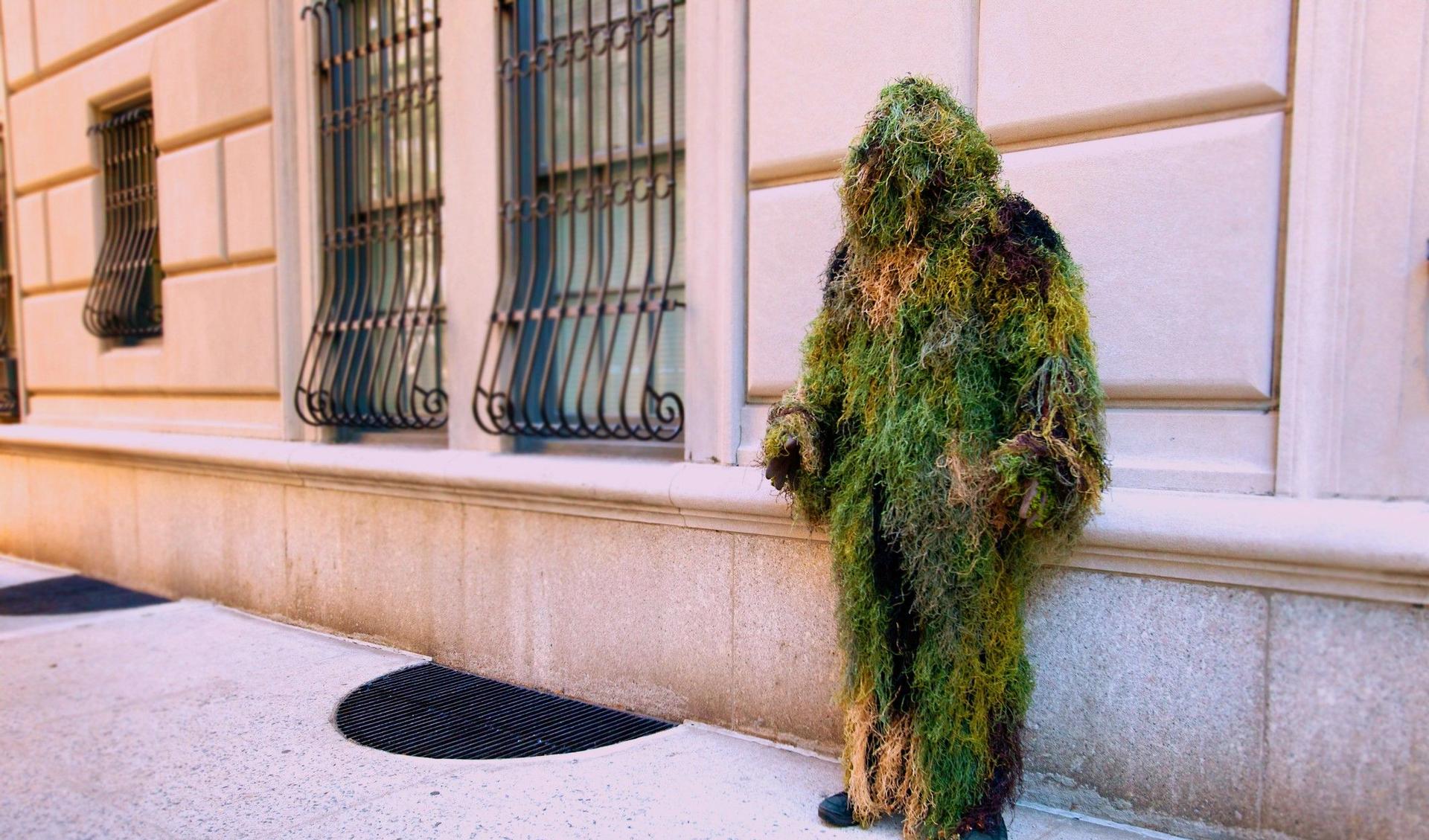 A man in a mass costume is standing on the street leaning at a wall