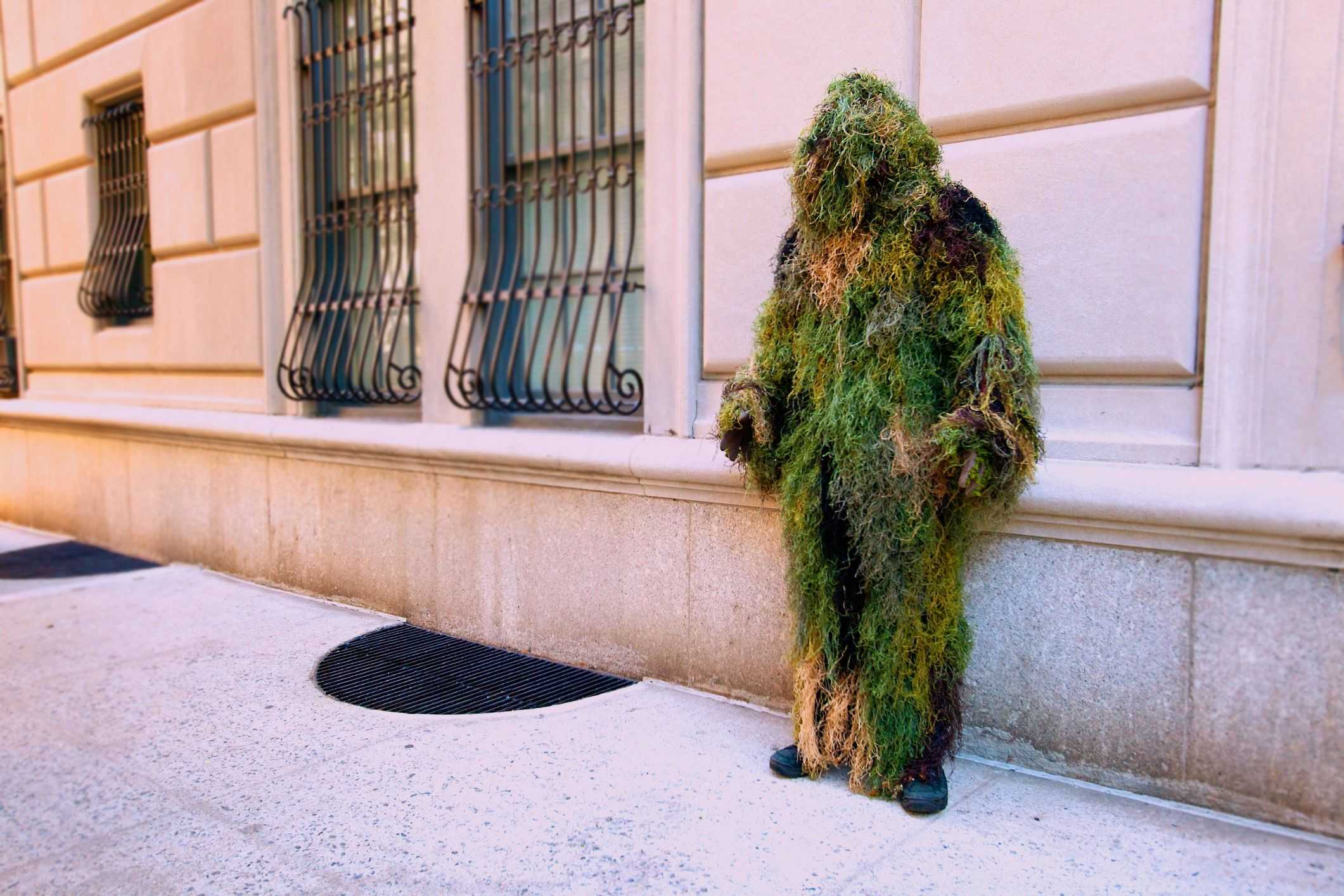 A man in a mass costume is standing on the street leaning at a wall