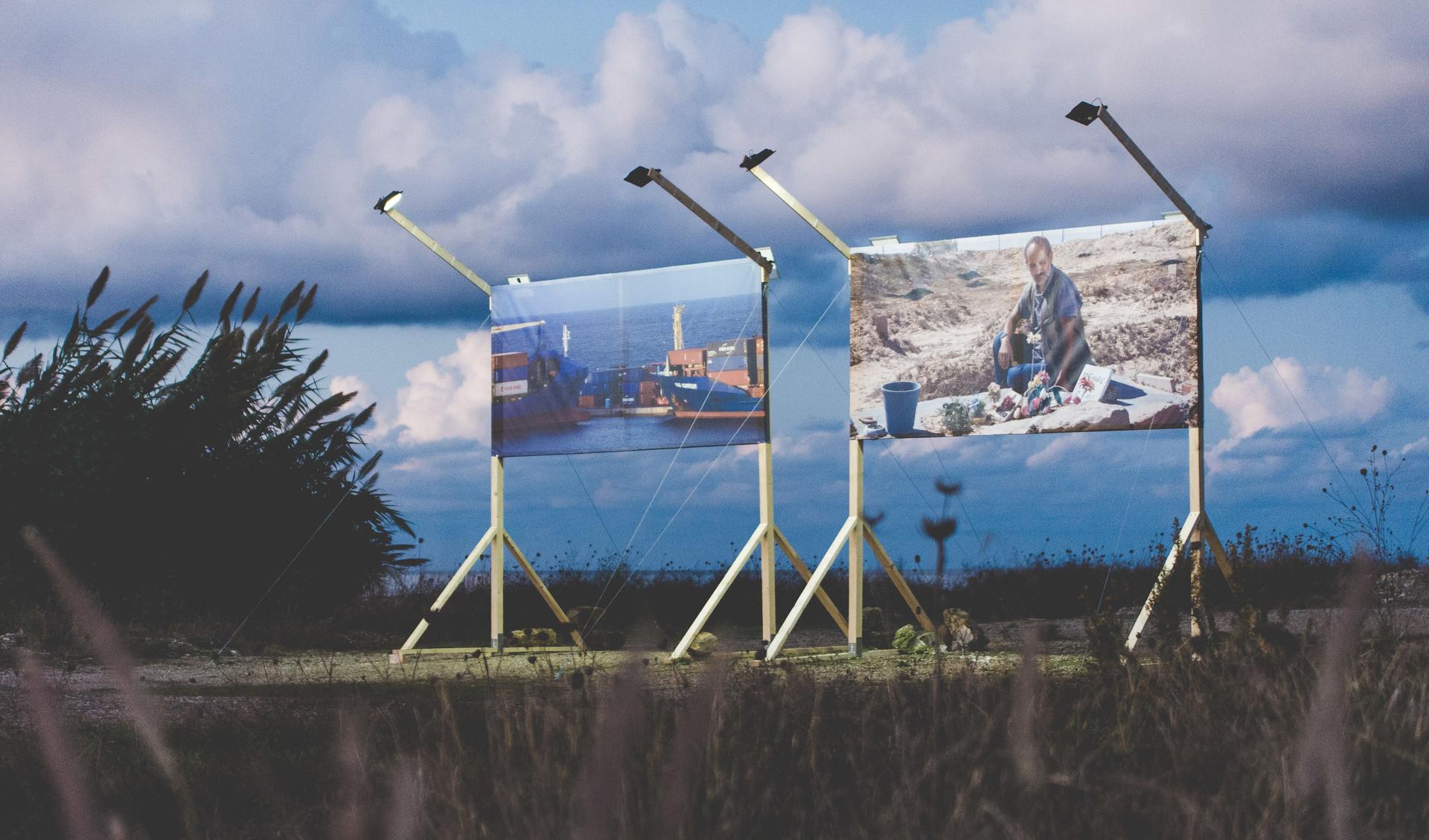 Two big billboaards are displaying pictures of a harbour and a person sitting in a rocky landscape