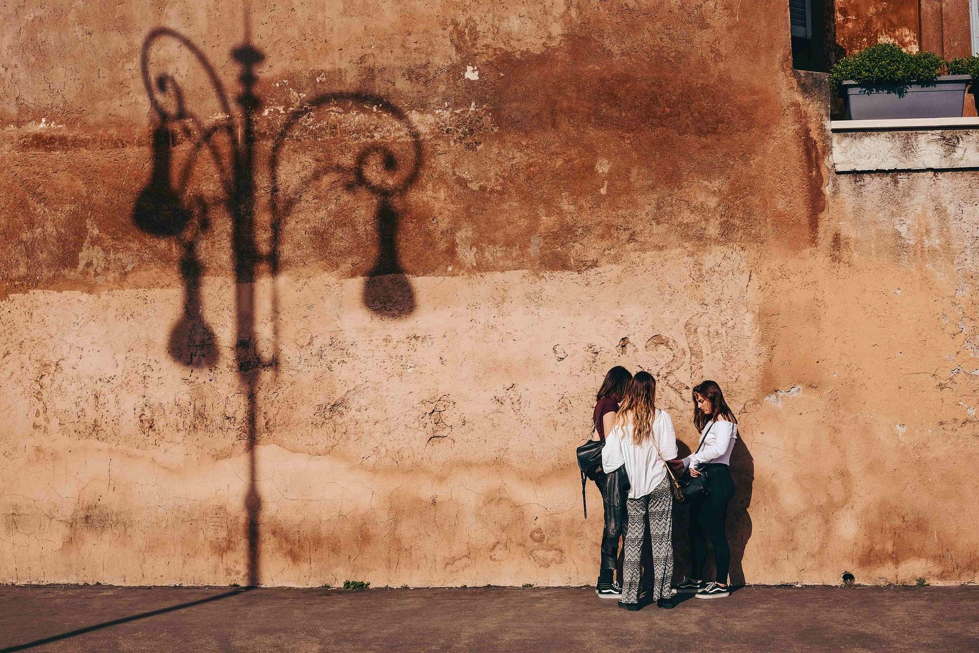 three young women are standing in front of a sunny wall and are talking to each other