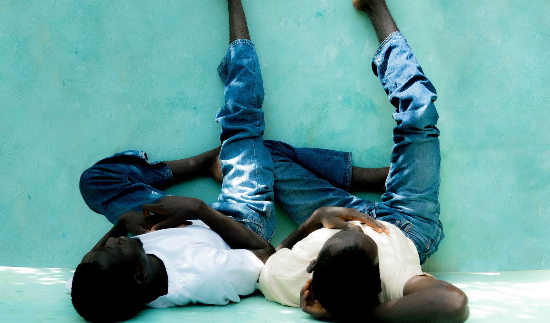 Two persons are sitting on the ground and leaning on a wall