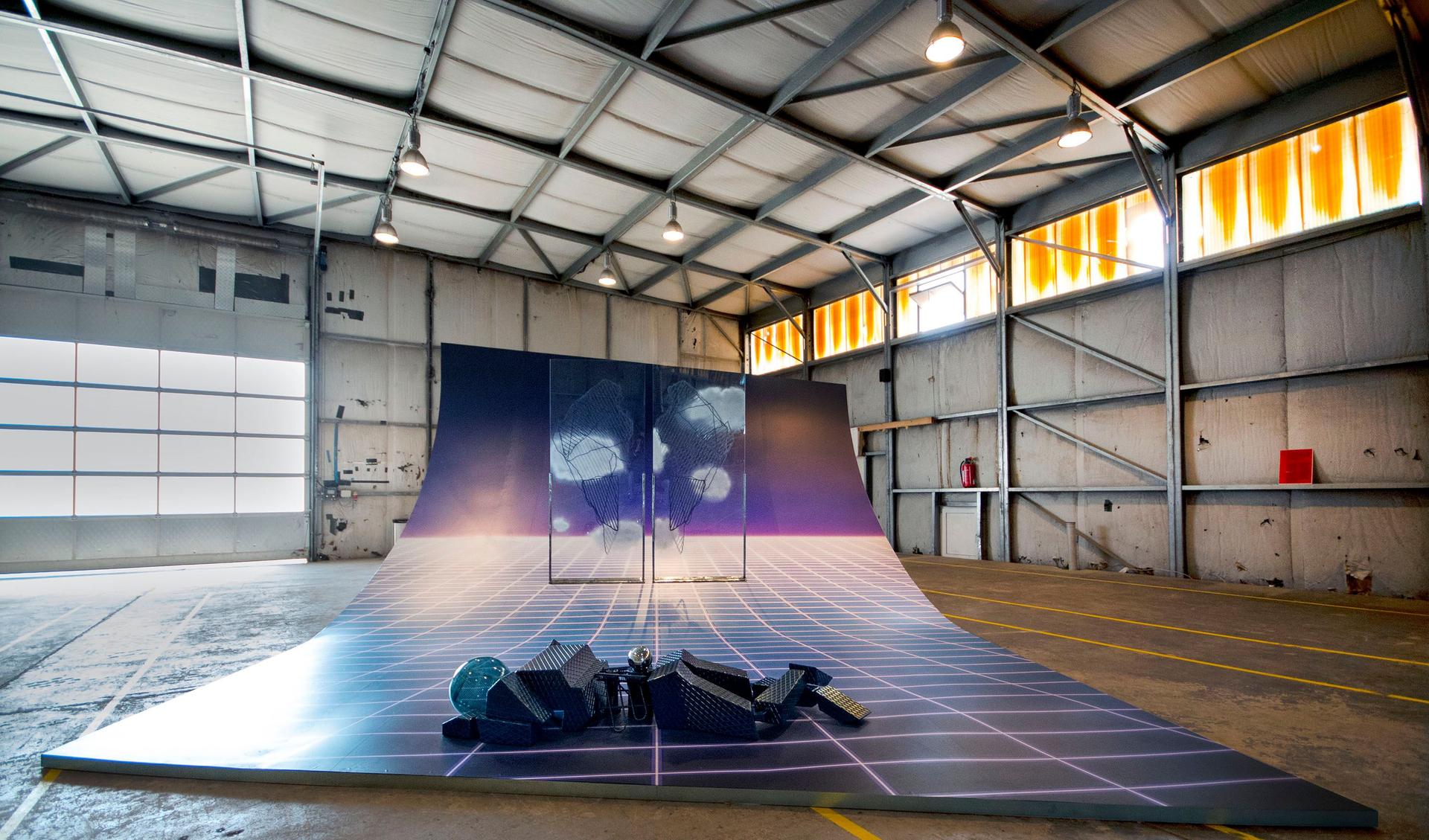 A huge art installation is displayed in an empty hangar.