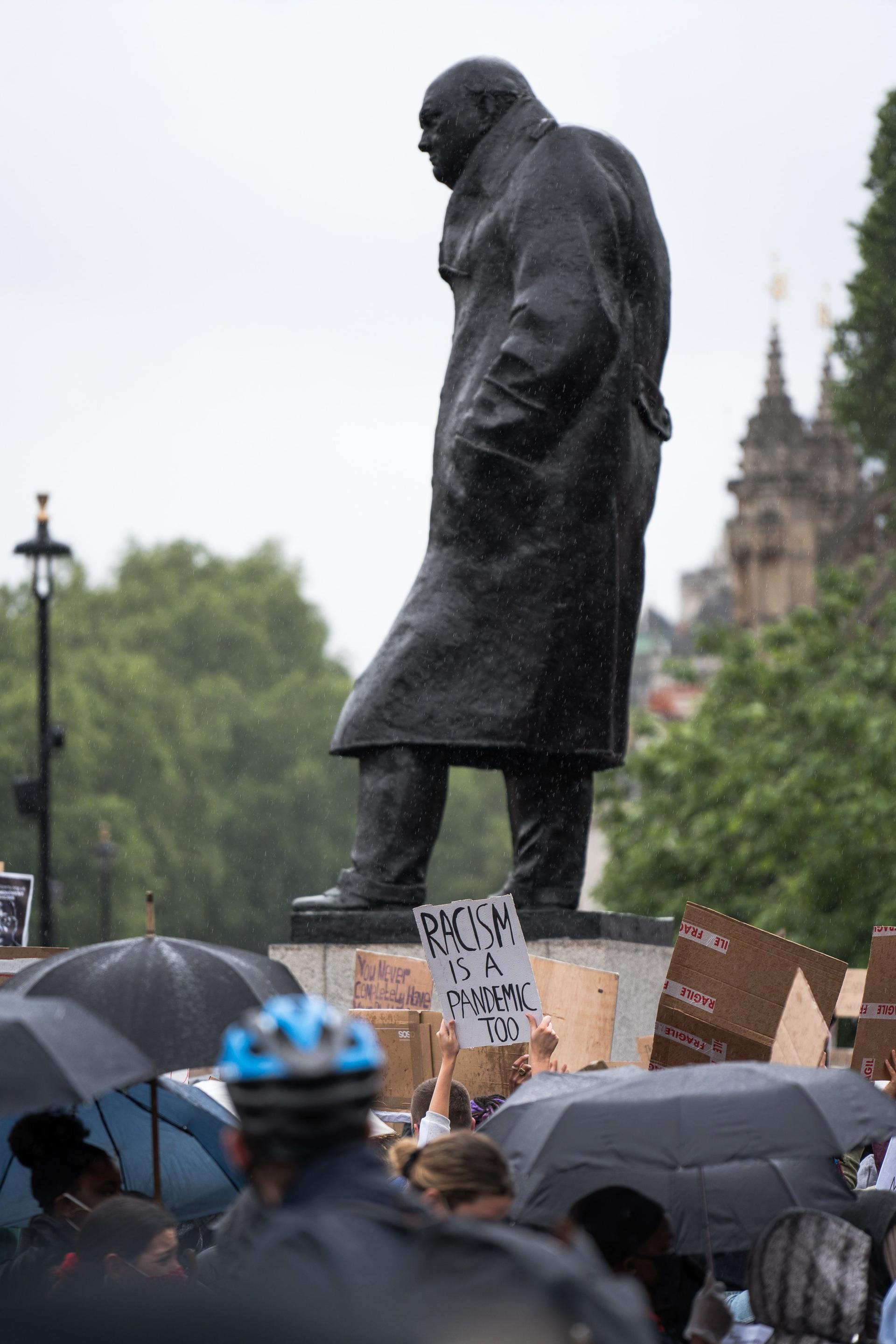 A statute of Winston Churrchill in London. Beneath the statute a protest is taking place.