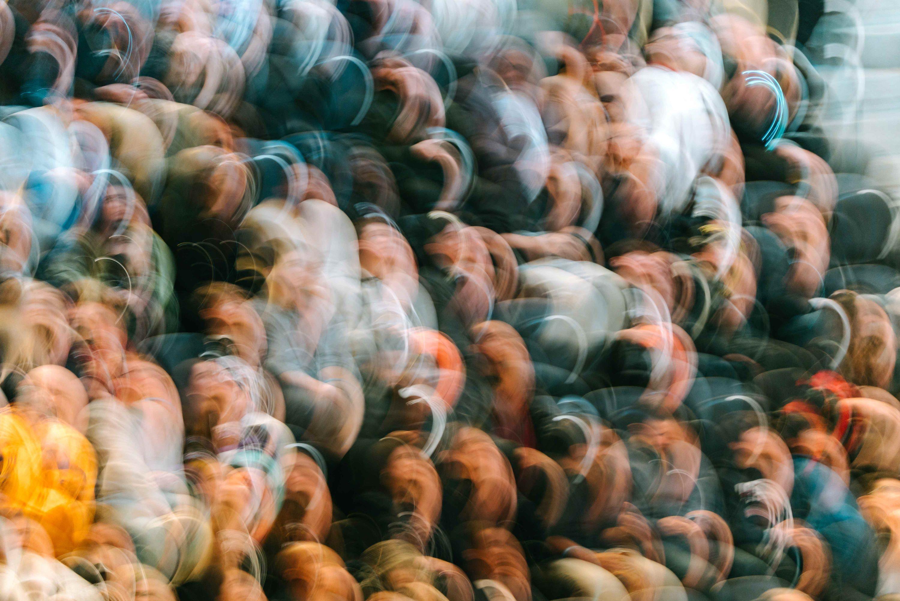 A crowd is standing and looking up. All faces are blurred