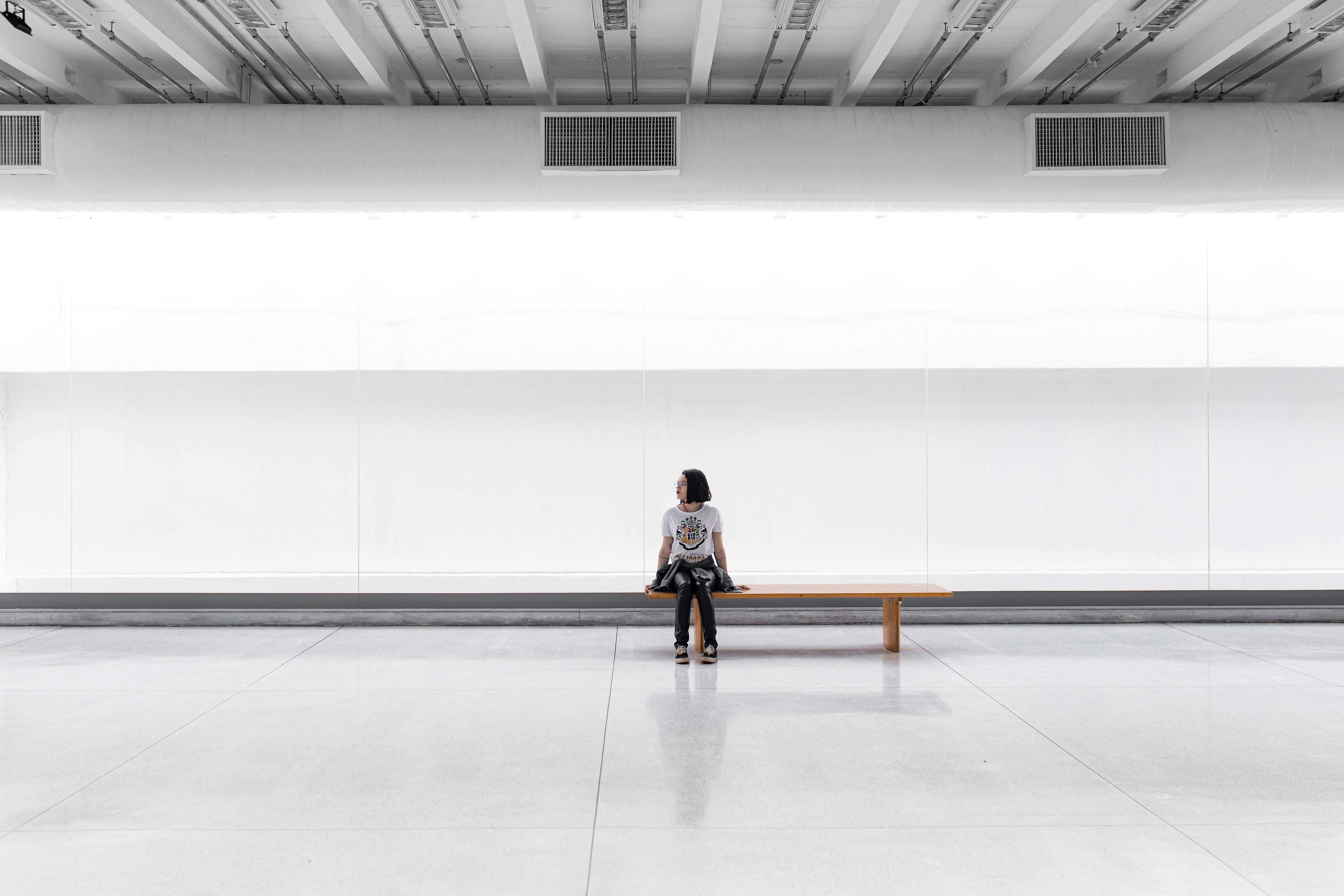 A person is sittin in a big white hall. She seems to wait for something