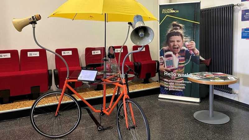 The polling booth reminds a bicycle with three wheels, speakers, touchpads and an yellow umbrella