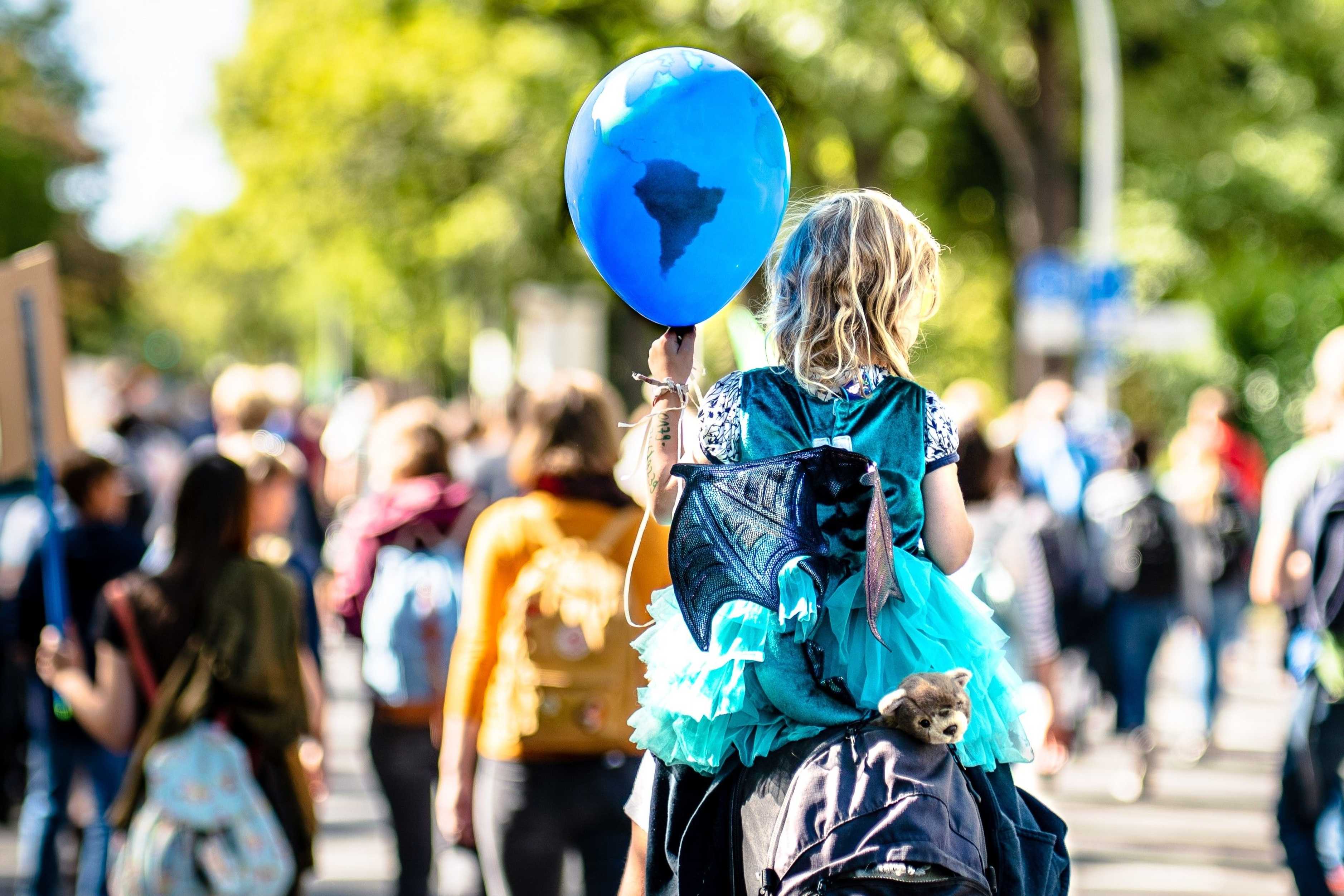 A demonstration - a child is sitting on the shoulders of a grown-uo person. It holds a ballon in its hands that looks like the earth but in blue.
