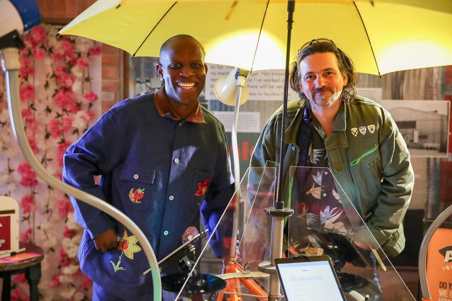 Two people are standing under an yellow umbrella.