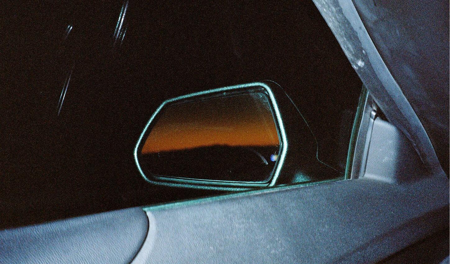 A rear mirror pictured from inside is showing a sunset