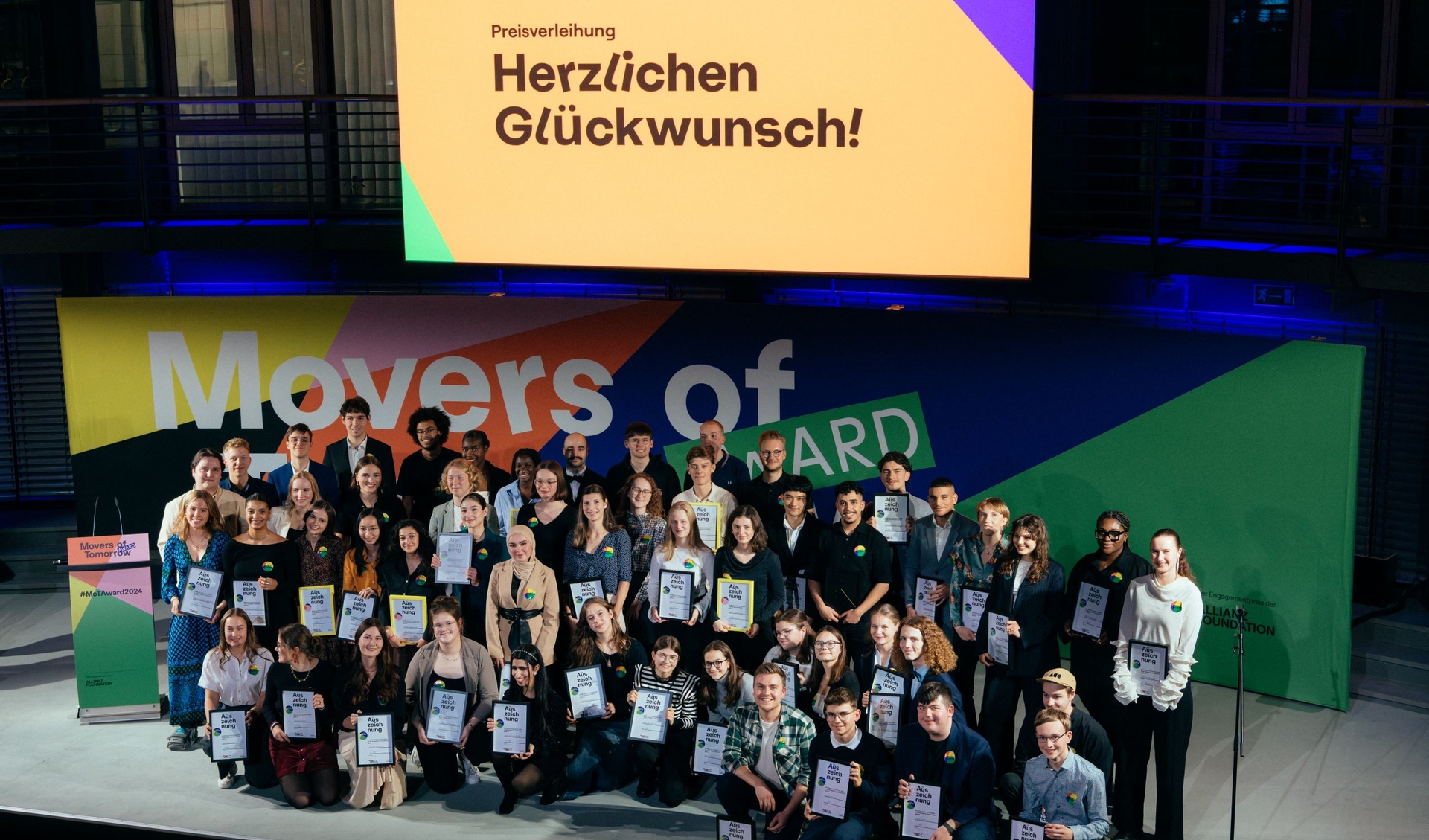 Young people are standing on a stage, holding their awards and look upwards