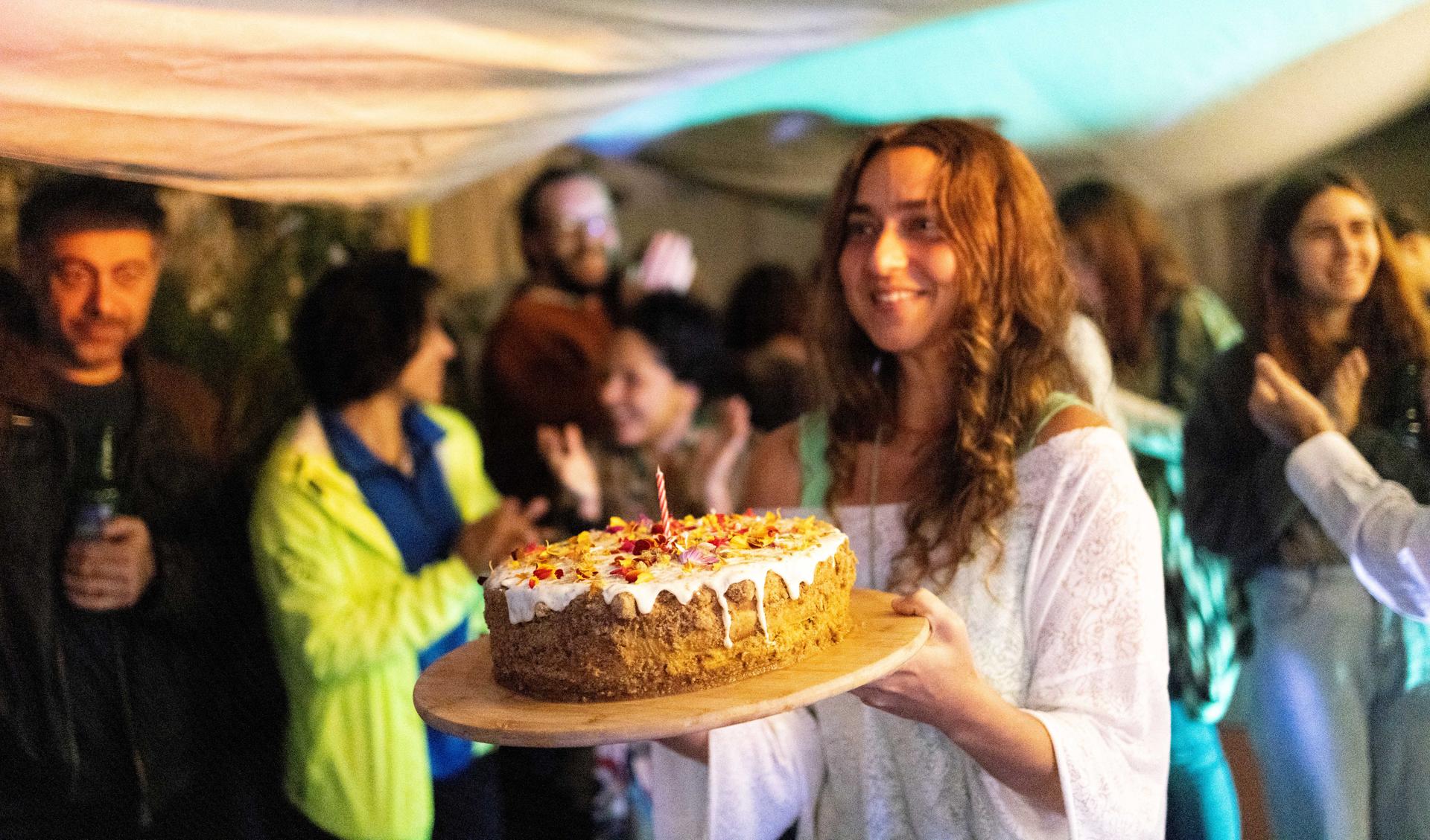 A person is carrying a birthday cake in a room that is full with people.