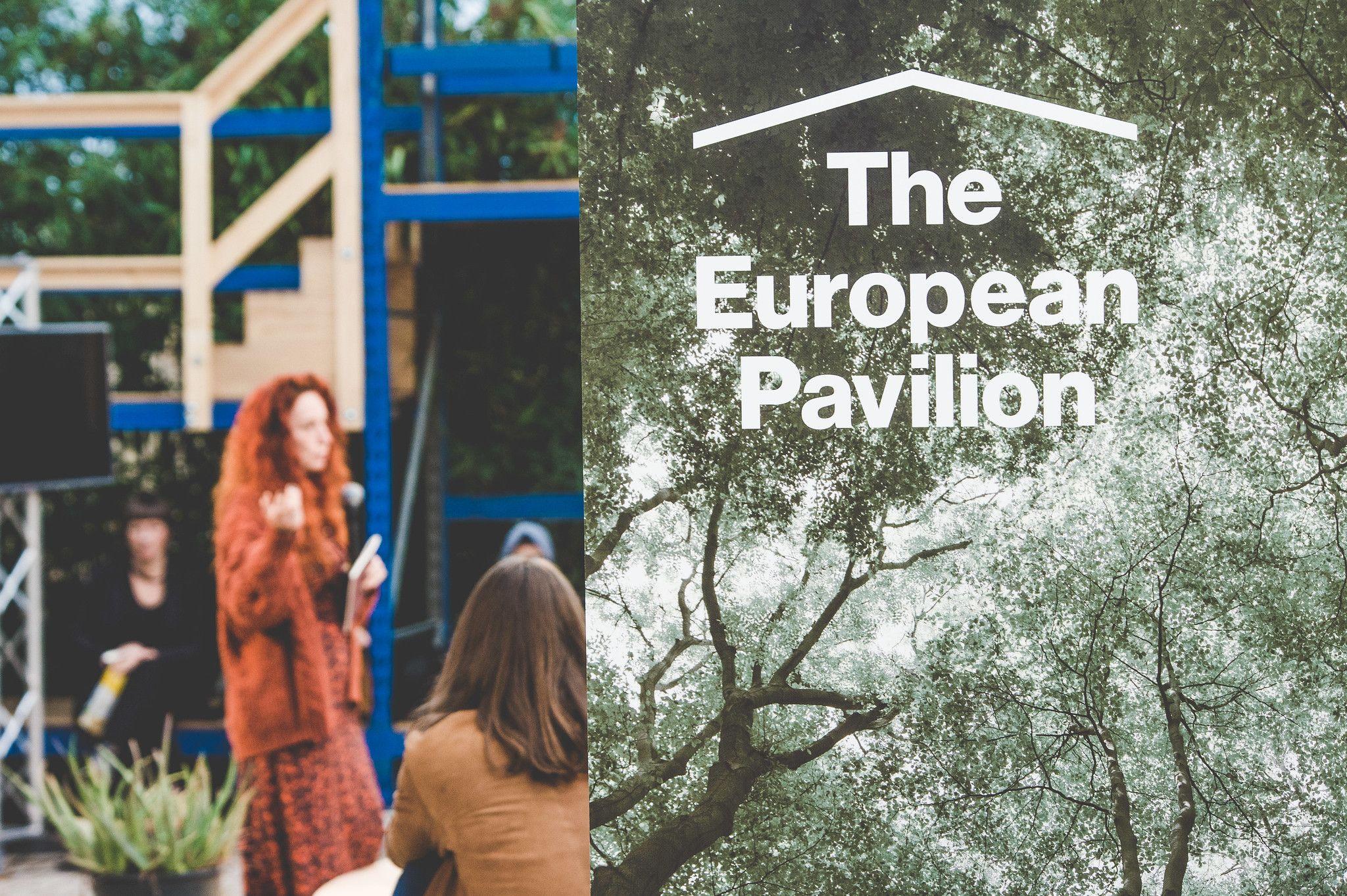 A Picture of a roll up with the inscription "European Pavilion" is pictured. In the background a person is speeking.