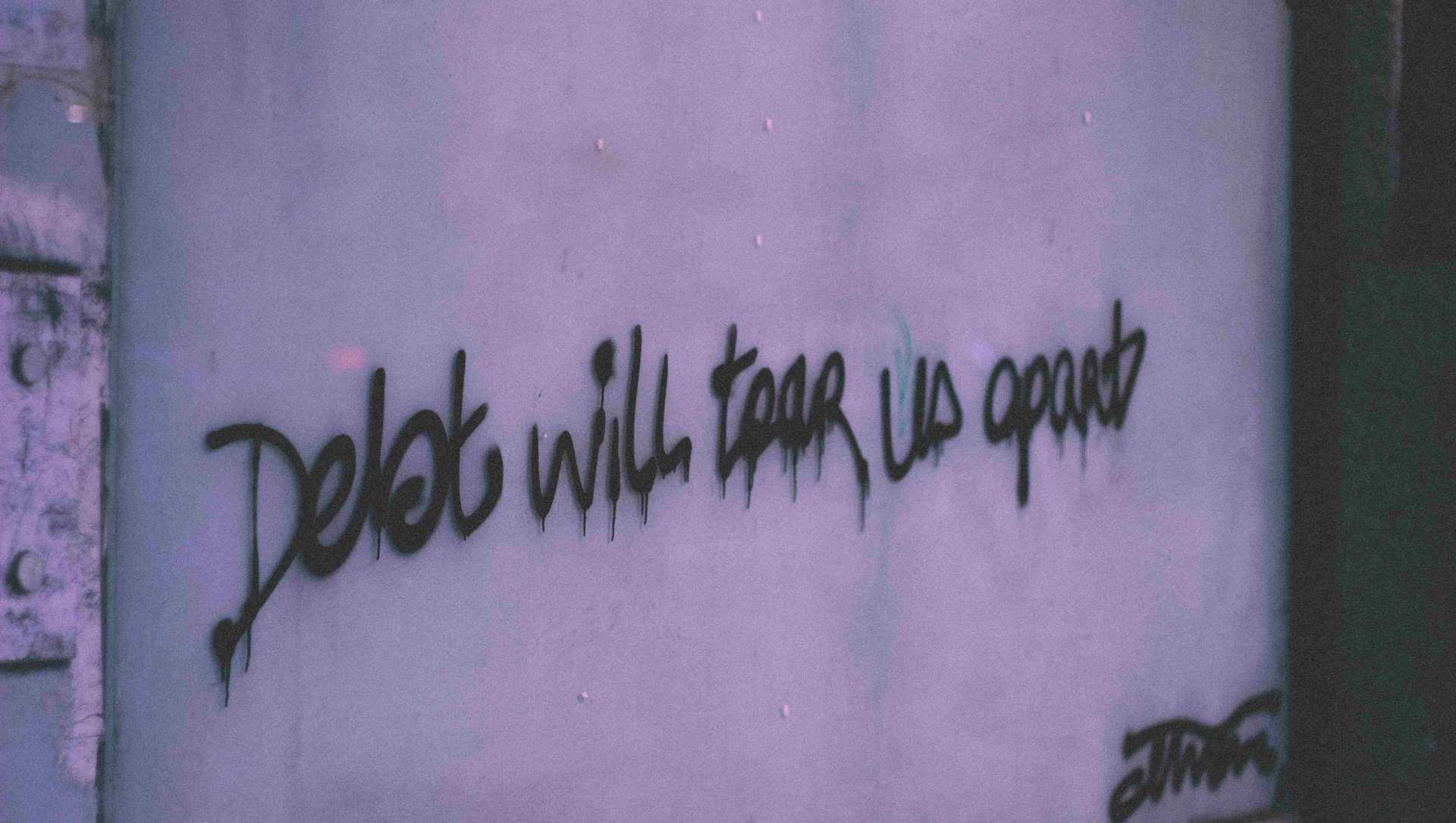 A writing on the wall says "Debt will tear us apart"