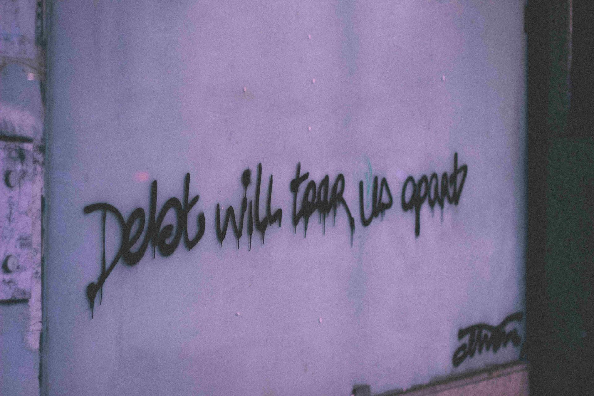 A writing on the wall says "Debt will tear us apart"
