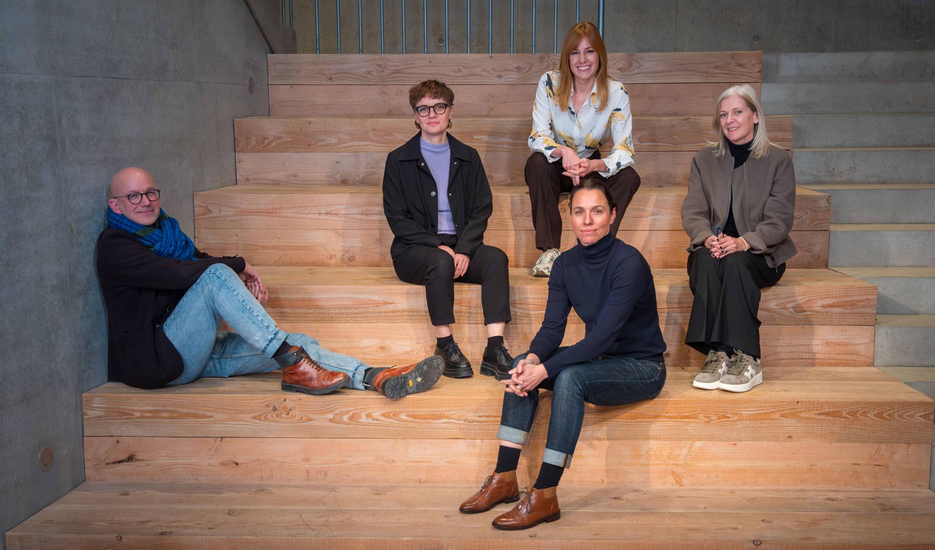 Five people are sitting on wooden steps.