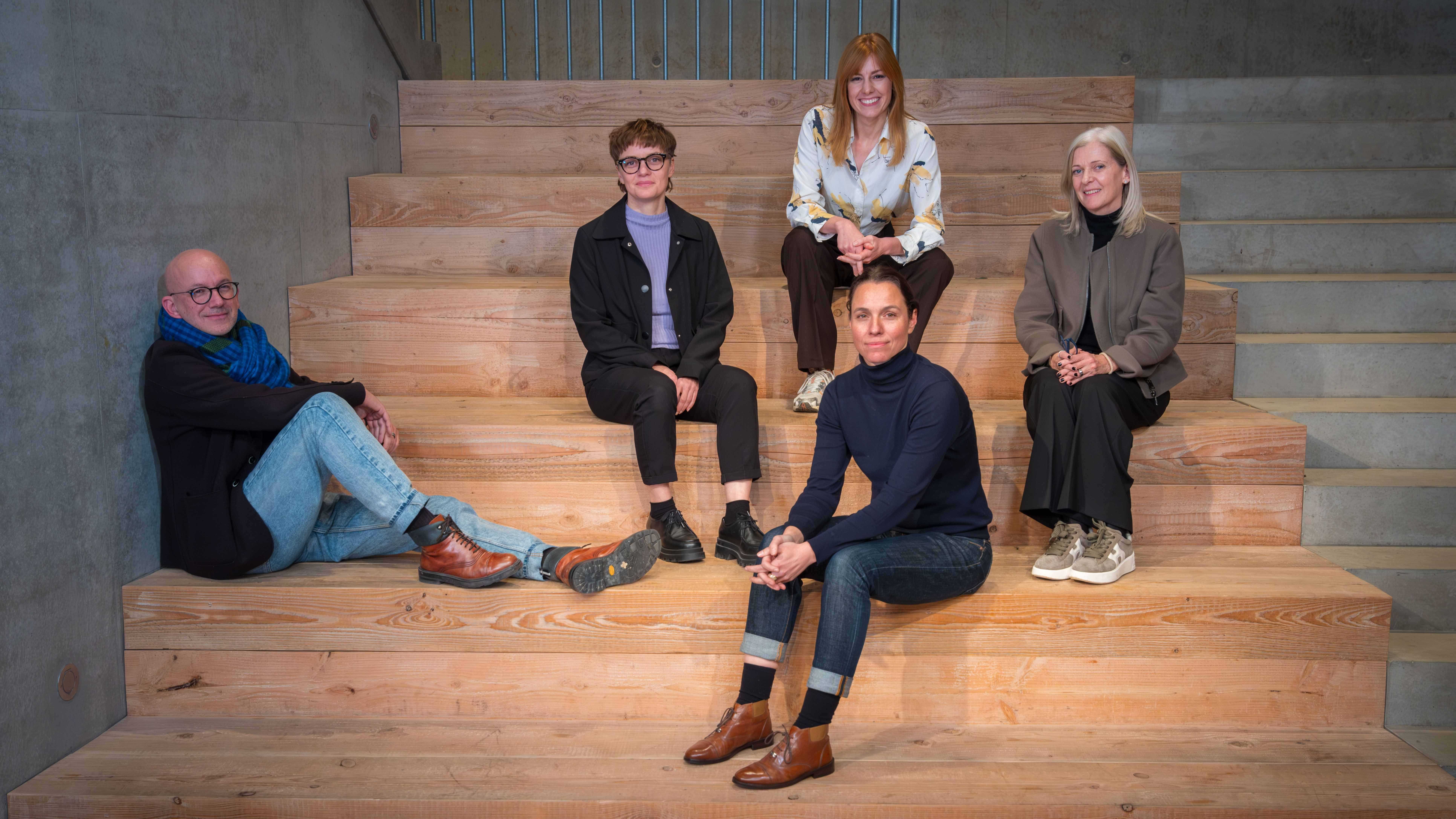 Five people are sitting on wooden steps.